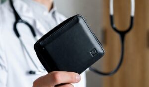 Keikkaääkäri pitää mustaa lompakkoa kädessään – symboloi keikkalääkärin korkeaa palkkaa